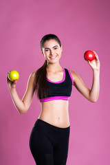 brunette girl with perfect figure smiles and Holds two apples apple on pink background