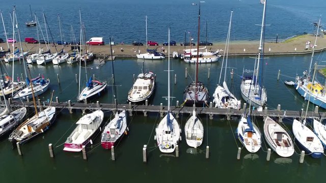Aerial bird view flying sideways left over marina showing docked recreational boats below both sail boats as motor boats als showing some parked cars in background beautiful day recreational harbor 4k