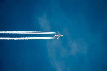Silhouette of plane flying against the blue sky. A trail of smoke behind