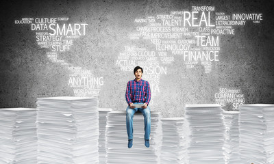 Attractive man sitting on pile of paper documents.