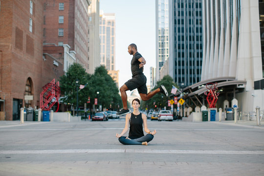 Muscular and athletic man jumping over a beautiful woman meditating in lotus pose