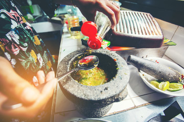 Close-up spoon's woman putting fish sauce on Stone mortar in the kitchen. Thai food concept.