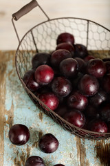 Ripe plums in a basket on a wooden background.