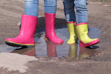 Children's legs in jeans in rain rubber boots standing in a puddle in the sun - 168785502
