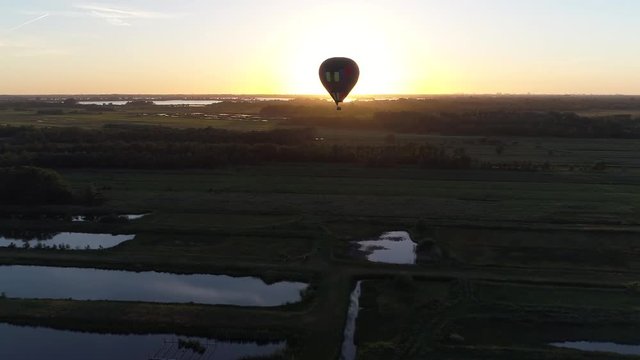 Aerial of hot air balloon bird view flying towards the sailing air balloon over nature reverse during sundown showing the bright late evening sun and the last light at horizon 4k high resolution