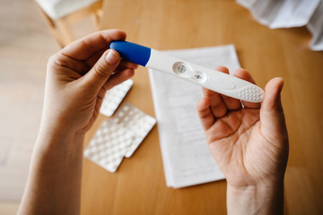 The girl holding a pregnancy test with a positive result on the background of the table with pills and a prescription. Two strips.