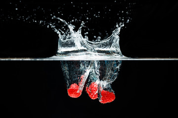 Three raspberrys falls deeply under water with a big splash.