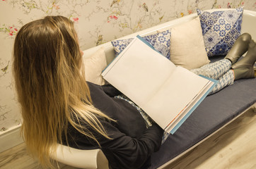 Mulher loira lendo livro em sofá estiloso. 