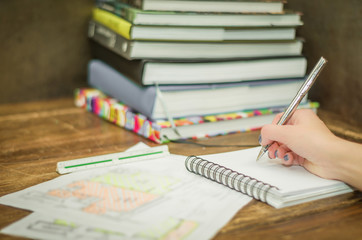 Escrevendo em caderno com livros ao fundo e material de trabalho