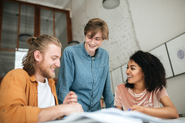 Portrait of young cheerful people discussing something in office. Two boys with blond hair and girl...