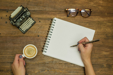 Mão de mulher escrevendo em caderno em branco com caneta, bebendo café, objetos de decoração