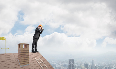 Engineer man standing on roof and looking in binoculars. Mixed media