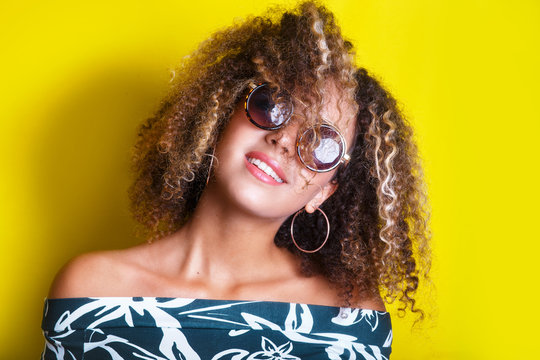 portrait indoors of a young afro american woman in sunglasses. Yellow background. Lifestyle. Casual clothing