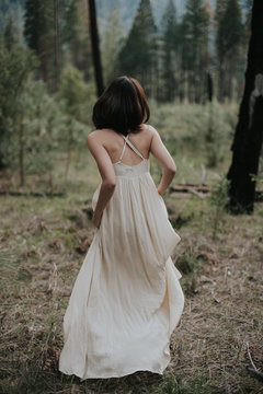 Adventurous bride in long bohemian dress walking through forest in Yosemite on her elopement