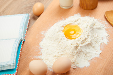 Flour heap and broken egg closeup for baking on a wooden background. Raw food and kitchen utensils.