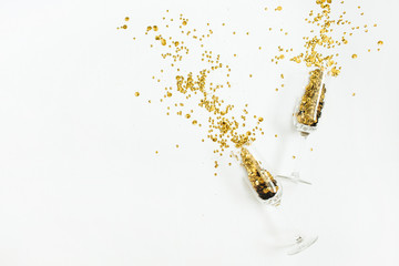 Glasses with golden confetti tinsel on white background. Flat lay, top view celebrate party concept.