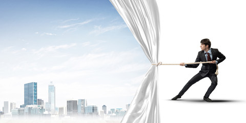 Obraz premium Young man opening white curtain and presenting modern city landscape