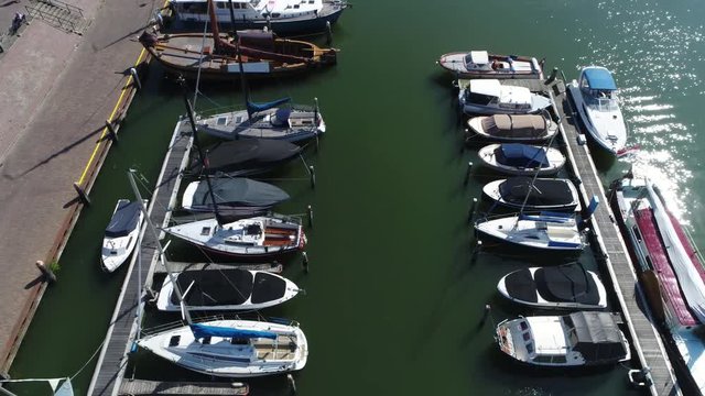 Aerial bird view flying over marina showing docked recreational boats below beautiful day bright reflection from sun seen in water and almost no people walking around at recreational harbor 4k