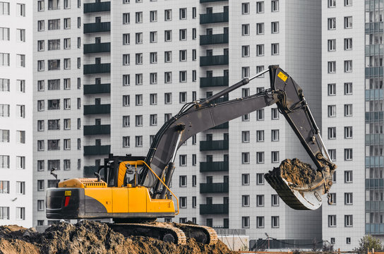 Excavator work on the ground on background of multi storey houses