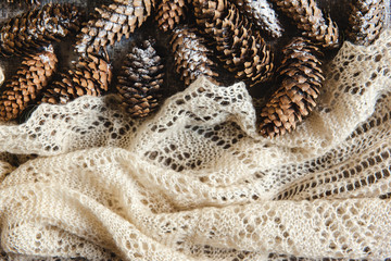 Winter holidays background of pine cones powdered with artificial snow and white downy shawl. Merry Christmas brown backdrop.