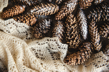 Winter holidays background of pine cones powdered with artificial snow and white downy shawl. Merry Christmas brown backdrop.