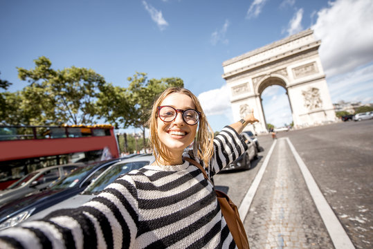 Fototapeta Young woman tourist making selfie portrait with famous Triumphal Arch on the background in Paris