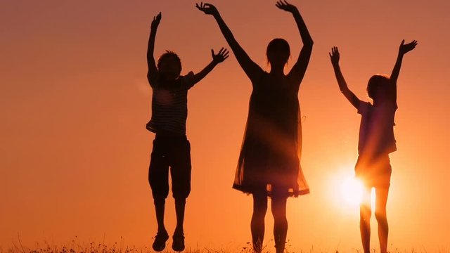 Mother and her children are jumping and waving their hands. The family is rejoicing and having fun at sunset.