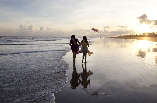 Mother and daughter enjoying running and flying kite in a beach