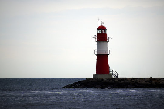 Red lighthouse on stones in the sea in bad weather against a gray sky, Warnemünde at the Baltic Sea, a popular holiday destination in Germany, Europe