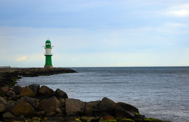 Green lighthouse on the stone shore at the sea against a cloudy sky, a navigation mark in...