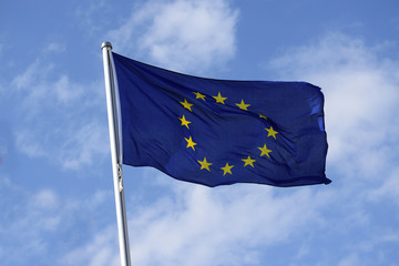 Flag of europe with yellow stars on a blue background as a symbol of the associated countries, fluttering in the wind against the blue sky with clouds on a sunny day