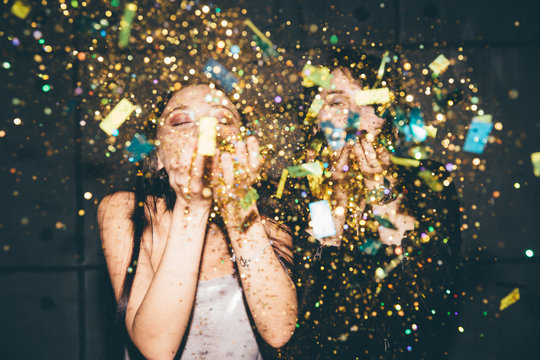 Two girl blowing golden confetti at camera