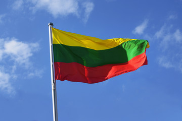 Flag of Lithuania with horizontal stripes in yellow, green and red, national symbol or sign of european country, fluttering in the wind against the blue sky with clouds on a sunny day