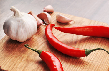 Hot chili peppers with the garlic bulb and cloves on a board
