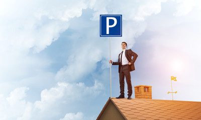 Young businessman with parking sign standing on brick roof. Mixed media