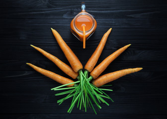Fresh carrot juice in a glass jar with handle on a black wooden table. Carrot smoothie in a glass mug with orange straw top view
