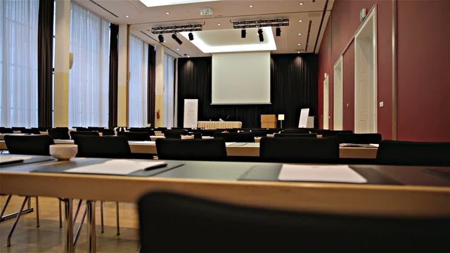 Big conference room with projector canvas from behind empty seat