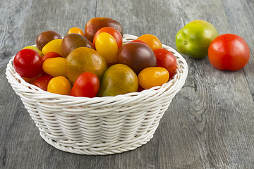 Colorful tomatoes of different sizes in white basket on gray wooden background