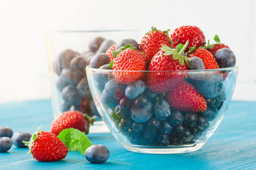 Blueberries and strawberry in glass bowl on wooden table background