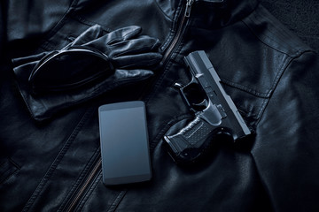 Gun, mobile phone and leather jacket on black background, criminality concept