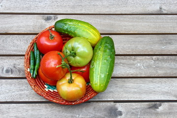 Red ripe Tomatoes and cucumber in a basket on a wooden background