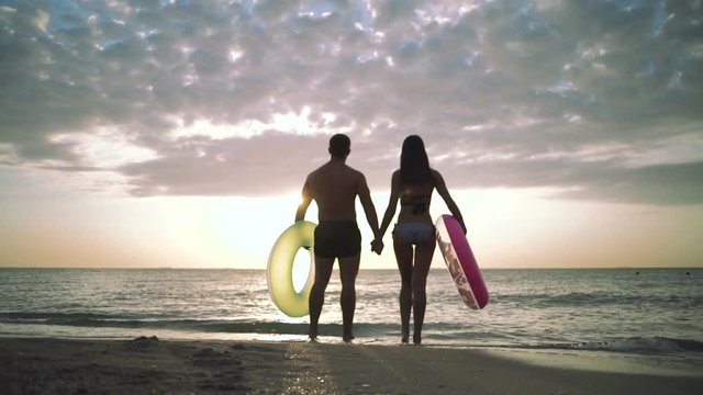 Silhouette of young couple on the beach with rubber rings during sunset