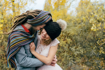 A cheerful couple goes crazy in. Bride in a knitted hat with a pompon and groom in colorful scarf are having fun. Wedding ceremony outdoors.