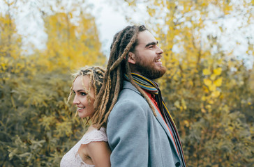 A cheerful couple stands back to back. Bride and groom with dreadlocks having fun on nature. Wedding ceremony outdoors.