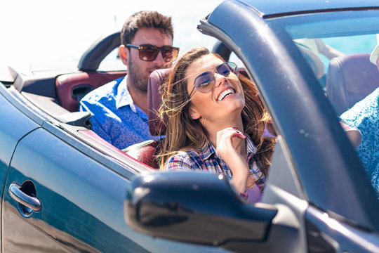 Group of happy young friends in cabriolet with raised hands driving on sunset