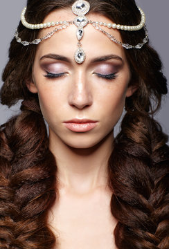 Beauty portrait of young woman with diadem. Brunette girl with long hair braids and day female makeup on gray background