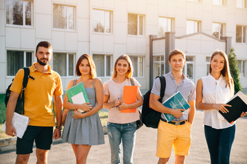 Portrait of group of happy students in casual outfit with books while standing on background of university