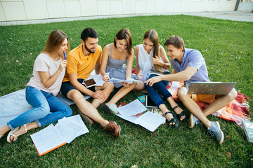 Group of cheerful students teenagers in casual outfits with note books and laptop are studying...