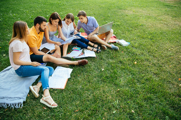 Group of cheerful students teenagers in casual outfits with note books and laptop are studying...