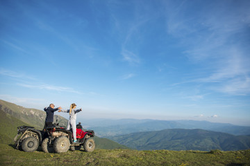 Beautiful couple is watching the sunset from the mountain sitting on quadbike